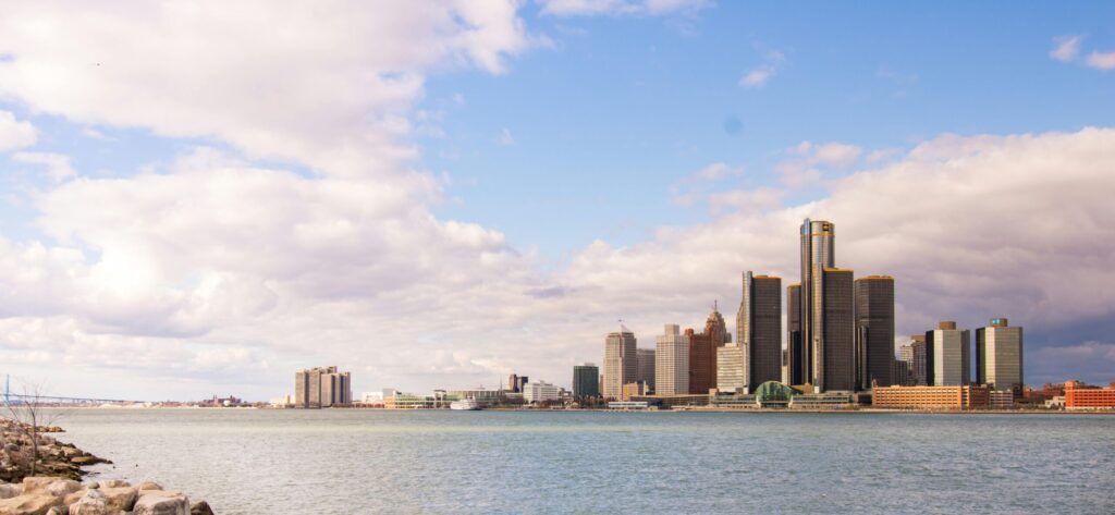 View of the Detroit skyline across the river on a clear day with rock-strewn waterfront.